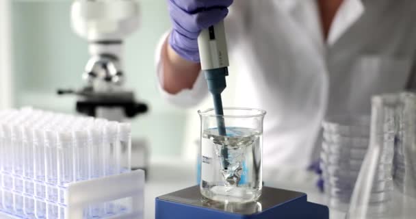 実験室での磁気回転子上のガラスからのピペットで水を取る化学者は 4K映画のスローモーションを閉じます 化学教育の概念 — ストック動画