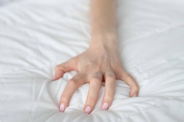 Strongly clenched female hand on sheet on bed. Intimacy of young woman on bed or bad dream concept