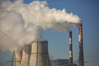 CHP cooling towers from which smoke is coming out against blue sky. Combined thermal power plant concept