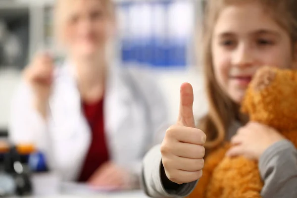 Little girl holding thumbs up in doctor office. Recommending quality healthcare services for children