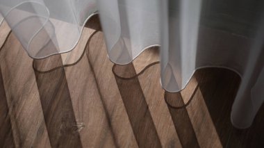 Sheer white tulle curtains and wooden floor. Sun rays of sunlight penetrate into dark room with shadows.