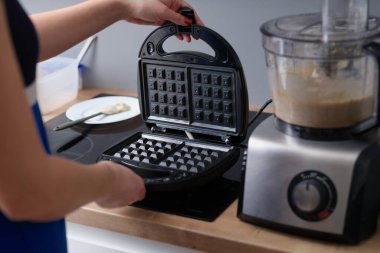 Woman opens waffle iron to make waffles in kitchen. Making waffles at home