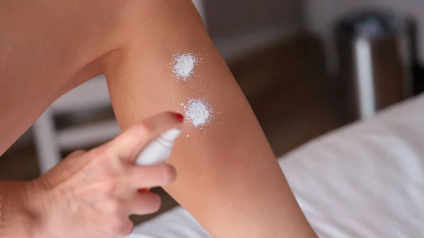 Woman applying moisturizer lotion spray on legs in home bedroom. Cream for and body sun protection spf
