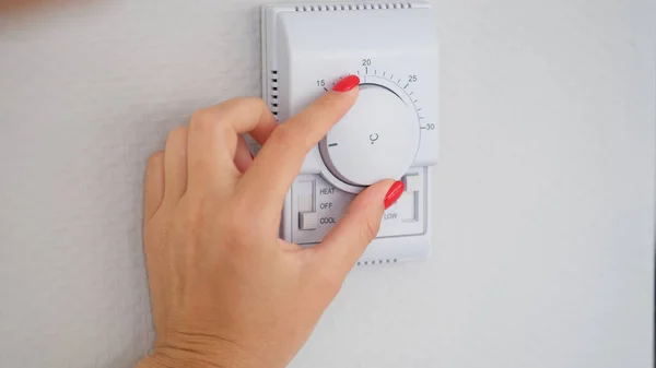 Woman hand adjusts or turns on wall temperature controller controller button. Climate control in room