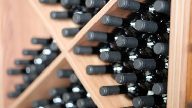 Various wine bottles are stacked on wooden racks. Elite collectible expensive wine in cellar