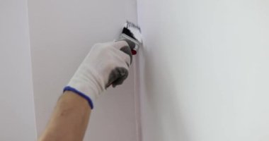 Hand holds brush and paints wall white. Home renovation and wall painting