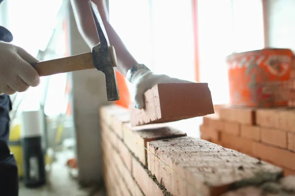Industrial worker builds interior walls using hammer and level to place bricks into cement. Detail of worker with tools
