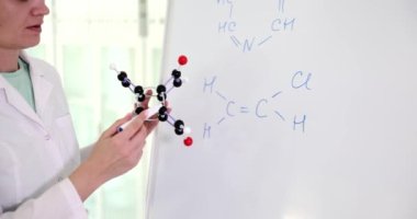 Woman scientist teacher holding molecular model and writing chemical compound on blackboard. Teaching in chemistry class