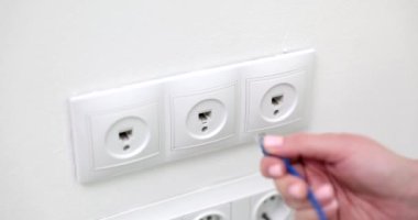 Closeup of woman hand inserting network cable into wall socket. Broadband network concept and home internet network