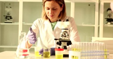 Scientist chemist takes sample from urine sample bottle and examines it under microscope. Biochemistry analyzes oil samples using microscope