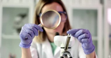 Chemist examines test tube with dark liquid or crude oil through magnifying glass. Chemical laboratory equipment toxic and poisonous substances