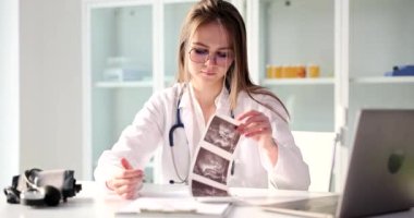 Hands of gynecologist doctor holding and examining ultrasound scan of pregnant woman. Results of examination of internal organs