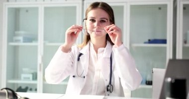 Portrait of doctor puts on glasses in clinic at workplace. Medical services insurance and medical care