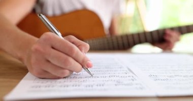 Gitarlı bir kadın yakın plan kalemle notlar yazar. İnternette solfeggio öğrenme kavramı, müzikal okur yazarlık.