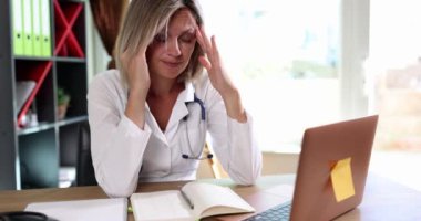 Kadın, masada oturan bir doktor başını tutar, yakın plan. Tıbbi personel yükle, işte stres yap.
