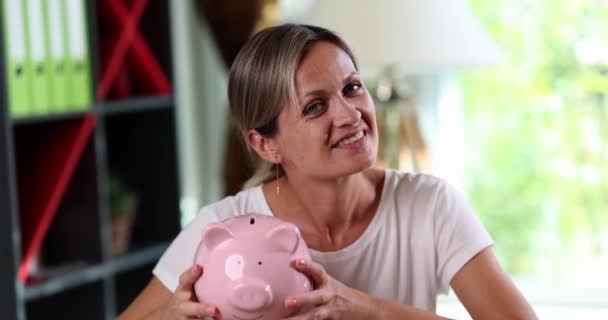 幸せな女性は彼女の耳 クローズアップの近くに貯金箱を振る 自己資金の積金の概念 — ストック動画