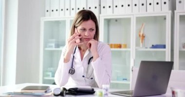 Woman doctor talking on mobile phone with patient in clinic 4k movie. Remote medical telephone consultation concept