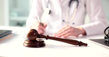 Gavel of judge lying on table in front of working doctor in clinic closeup 4k movie slow motion . Criminal liability of medical personnel in case of medical negligence concept