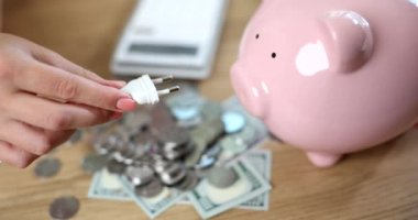 Hand inserting electric plug into piggy bank with money closeup 4k movie slow motion. Economic crisis of saving electricity concept 
