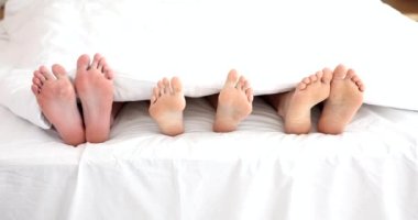 Female and two pairs of male legs lying under blanket at home 4k movie slow motion. Sexual fantasy threesome concept 