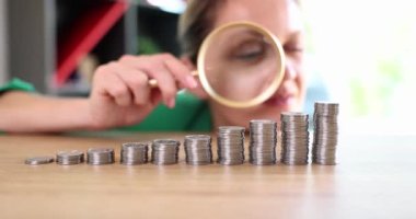 Businesswoman looking through magnifying glass at coins in ascending order 4k movie slow motion. Business earning strategy concept 