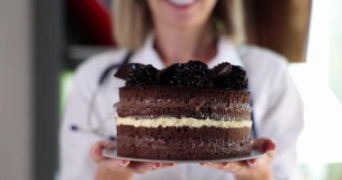 Woman doctor holding appetizing tasty cake closeup 4k movie slow motion. Medical consequences after overeating concept 
