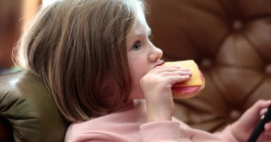 Child lying on sofa and eating delicious sandwich with sausage and cheese 4k movie slow motion. Proper nutrition in children concept 