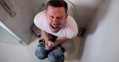 Young man sitting on toilet and screaming in pain during bowel movements 4k movie slow motion. Constipation as cause of hemorrhoids concept 