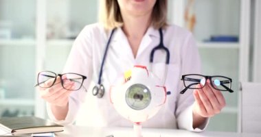 Doctor ophthalmologist giving patient choice of glasses for vision in front of artificial model of human eye. Selection of glasses concept