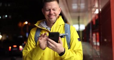 Male courier looking at mobile phone and waving to customer for food delivery 4k movie slow motion. City map in mobile apps concept