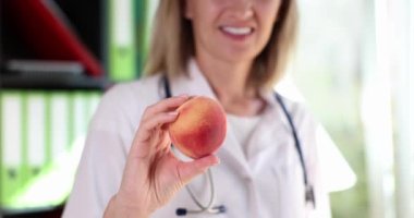 Woman doctor nutritionist therapist offering fresh peach. Vitamins healthy food and diet