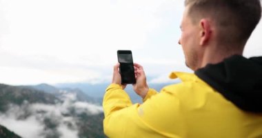 Tourist man photographs top of hill and beautiful landscape on top of mountain. Traveler blogger filming natural landscape