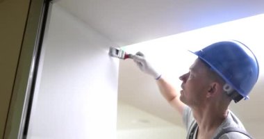 Erkek müteahhit, duvarı fırça ile beyaza boyuyor. Daire kavramında iş bitirme