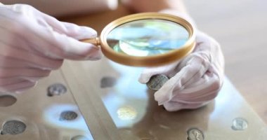 Numismatist in gloves examines collection of Georgian coins through magnifying glass. Collecting, valuation and sale of antique coins