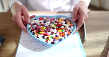 Doktor kardiyolog elinde bir kalp plakası ve bir sürü ilaç tutuyor. Uyuşturucu bağımlılığı semptomları ve kalp ilacı seçimi konsepti