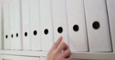 Woman searches and pulls out white folder with documents. Document search and business documentation archive