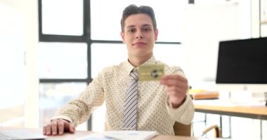 Smiling man sits in office and shows credit card. Banking and online payment