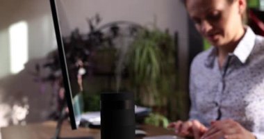 Working humidifier against background of working woman working in office. Healthy office environment and humidifier steam