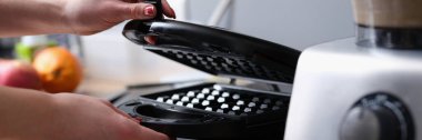Kadın mutfakta elektrikli waffle ızgarası açıyor. Elektrikli waffle ızgarası konseptinde waffle pişirmek