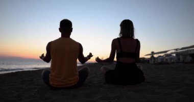 Çiftler sabahları veya akşamları plajda yoga yapıyor. Uyum dengesi ve uyum.