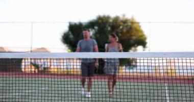 Two friends, man and woman, are walking along tennis court. Couple about to play friendly tennis match