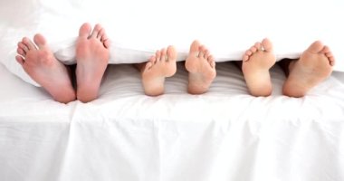 Three people under blanket with bare legs in bed. Group sex and lovers