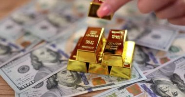 Hand puts gold bar on dollar bills. Investing in gold and financial income growth