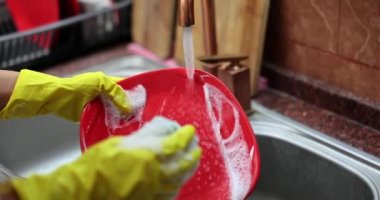 Sarı koruyucu lastik eldivenli eller kırmızı tabağı yıkıyor. Bulaşık konsepti
