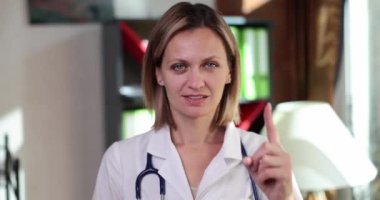 Woman doctor showing thumb up and attention gesture in medical office. Health alert attention and medical advice