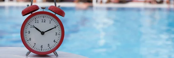 Red alarm clock for ten oclock near pool in hotel or spa center. Summer vacation tourism and relaxation concept