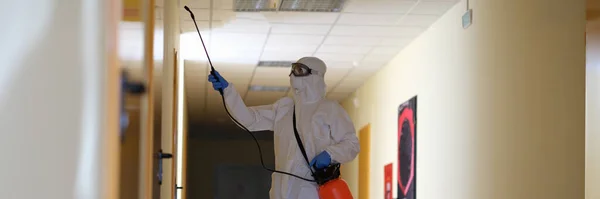 Person in protective suit with disinfectant cleaning public area in during pandemic. Carrying out disinfection and antiviral treatment concept