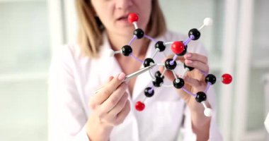 Kadın bilim adamı elinde moleküler yapı modeli gösteriyor ve öğrencilerle iletişim kuruyor. DNA kimyasal araştırma eğitimi