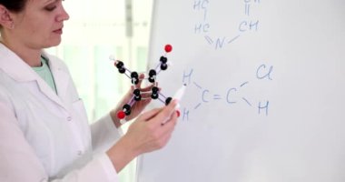 Female chemist holds molecular model and draws chemical formulas on whiteboard. Chemical research education and scientific experiments