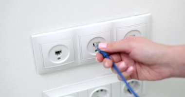 Closeup of woman hand inserting network cable into wall socket. Broadband network concept